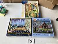 Three jigsaw puzzles with packaging on table: a Frank Lloyd Wright inspired design, a house and tree scene, and a cat on a windowsill.
