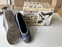 Two boxed Shoe Slotz shoe storage units next to a pair of women's shoes on a cardboard box background