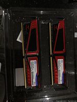 Two DDR4 RAM sticks with red and black heat spreaders inside plastic packaging.