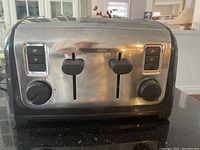 Front view of four slice Black & Decker toaster showing two sets of slots, adjustable dials, and levers. Stainless steel with black trim. Scratches visible on surface.