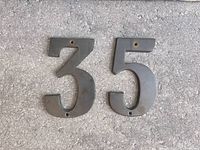 Front view of brass numbers 3 and 5 showing mounting holes and tarnished surfaces