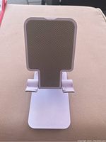 Front view of white plastic cell phone stand with padded backrest and hooks to hold phone securely.