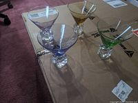 Four different colored martini glasses arranged in a square pattern on a cardboard surface, colors are amber, purple, blue, and green.