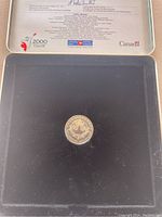 Silver commemorative coin displayed inside the black tray of the silver presentation case with printed text and signatures on the case lid.