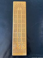 Top view of the wooden cribbage board showing the peg holes arranged in oval tracks and scoring boxes with visible scratches and wear on the wood surface.