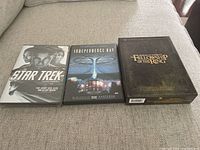 Photo of three DVD movies laid out on fabric surface showing Star Trek, Independence Day and Lord of the Rings extended edition.