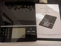 Photo of the Wasserstein electronic food scale on a surface with numeric keypad, LCD screen, and control buttons along bottom right edge. Includes instruction manual.