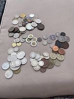 Overview of many assorted foreign coins spread on a surface showing variety in size and color.