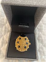 Ladybug-shaped gold-tone expandable ring with black spots inside its box.
