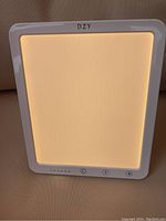 DZY light therapy lamp emitting warm white light with visible control buttons and brand logo.