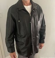 Front view of a man wearing a black leather jacket showing zipper and pocket details, and the style of the collar and sleeves.