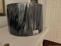 Lampshade wrapped in clear cellophane, showing deep matte navy blue fabric, photographed from side angle.