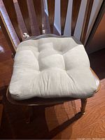 Cream-colored side of reversible chair cushion shown on wooden chair with ties visible.