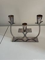 Photo of a silver metal candle holder designed for three candles with curved arms and rectangular base.