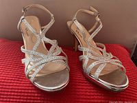 Front view of the pair of silver Nina high heel shoes showing sparkly rhinestone straps and open toes, placed on red textured fabric.