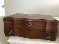 Closed view of the wooden jewellery box showing curved wooden front and brass hardware locks.