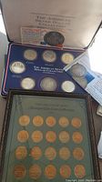Both coin collections displayed together: silver dollar case in blue tray and framed bronze-tone car medallions with COA inserts