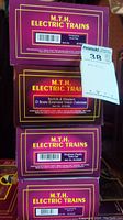 Photo of four purple MTH Electric Trains boxes showing product labels for Pennsylvania Snow Plow, Norfolk & Western Extended Vision Caboose, Southern Pacific Tank Car, and Sunoco Tank Car.