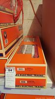 Stacked Lionel train boxes showing original packaging with orange and white colors. Two different model train flatcars visible through clear box windows.