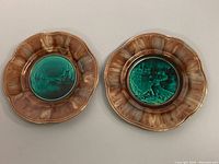 Two scalloped-edge ceramic plates side by side showing brown mottled edges and embossed green scenic centers