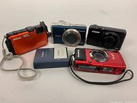 Overview of four cameras (Nikon, Olympus, Canon SX200 IS, Canon S90) and Canon charger battery