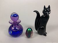 Full view of all three items: Murano glass cat sculpture, Caithness blown glass perfume bottle, and iridescent egg paperweight.