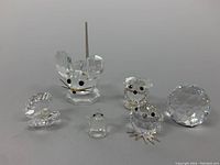 Six Swarovski crystal figurines arranged on a gray surface showing mouse, birds, swan and a large faceted round crystal piece.