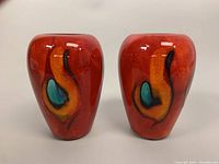 Front view of two red Poole 'Peacock' pottery vases showing the abstract feather design.