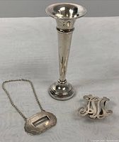 Photo showing the sterling silver bud vase, the decanter label on chain, and the monogrammed Birks money clip together on a table.