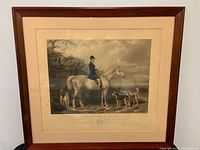 Overall view of framed engraving on wall, showing brown wood frame, cream mat, and artwork.