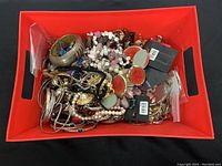 Photo showing assorted jewelry items in a red container including necklaces, rings, and bracelets.