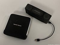 Both speakers shown together on a surface, Harman/Kardon Esquire and Bose SoundLink Mini with USB cable attached.