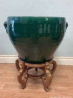 Side view of large green glazed planter pot on wooden stand