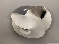 Top and side views of the polished stainless steel fruit bowl showing its flowing, curved design and reflective surface with minor wear.