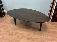 Front angle showing dark wood boomerang-shaped coffee table on light wooden floor against light blue wall.