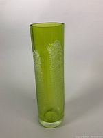 Full view of tall green cylindrical vase with textured white abstract design on surface.