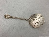 Full view of the sterling silver serving spoon showing ornate handle and pierced bowl.