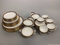 Full set view showing stacked plates, double handle soup bowls, and teacups with saucers arranged.
