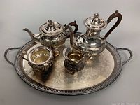 Silver plated tea set arranged on an ornate oval tray showing coffee pot, teapot, creamer, and sugar bowl with decorative repousse pattern.