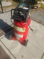 Photo of the red Husky 22 gallon air compressor showing full unit with wheels and handle on outdoor carpet.
