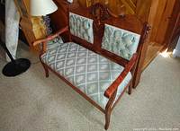 Antique wooden settee with blue-gray patterned tufted upholstery, carved wood details, armrest, and matching pillows