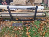 Full view of black metal back rack with horizontal bars and the words "BACK RACK" on the crossbar, laying on grass with fallen leaves.