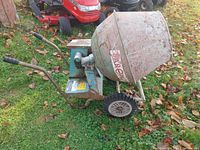 Side view of the old gas powered cement mixer showing handles, wheels, and motor area with rust and wear.