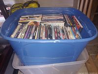 Blue plastic bin filled with DVDs arranged upright and stacked horizontally in two layers