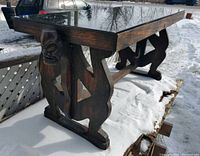 Side view showing detailed carved face and figure on wooden leg supporting smoked glass top