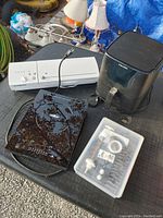 Overall view of lot items on a gray surface showing induction cooktop, deep fryer, white appliance with knobs, and plastic box with accessories.