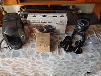 Wide view of kitchen lot items including cookware set box, black Hamilton Beach juicer with attachments, new creamer set box, and dust-covered appliances.