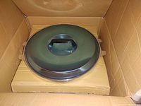 Stainless steel lid with handle placed on top of a box inside the packaging.