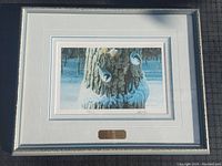 Framed print showing winter scene with owls on a tree trunk, surrounded by white and grey mat and silver frame.