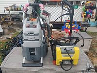 Two pressure washers on a table outdoors, one large Briggs & Stratton and one smaller yellow Karcher unit.